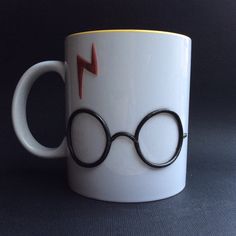 a harry potter mug with glasses and lightning bolt painted on the side, sitting on a black surface