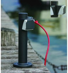 a red cord connected to a black pole on a dock next to the water with boats in the background