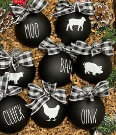 black and white christmas ornaments with farm animals on them in a box next to pine cones