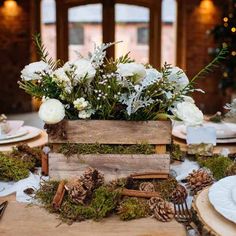 a wooden box filled with white flowers and greenery on top of a dining table