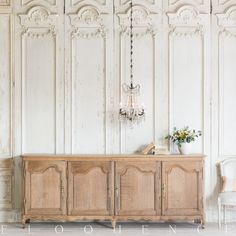 an old wooden sideboard with chandelier hanging from it's ceiling in a white room