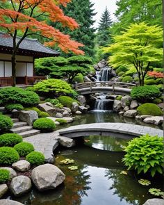 a small pond surrounded by rocks and trees in the middle of a garden with a bridge over it