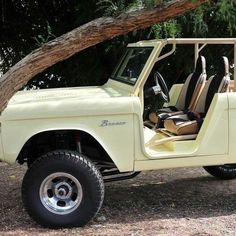 an old yellow jeep is parked under a tree with its doors open and the seat up