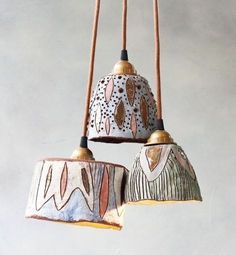 three hanging lights made out of clay with designs on the lampshades and wood cords