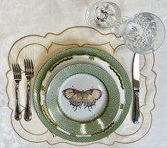 a plate with a butterfly on it next to silverware and wine glasses in front of a white tablecloth