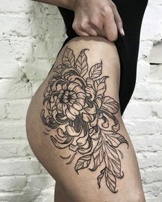 a woman's thigh with flowers and leaves tattoo on her leg, while she is holding