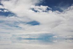 the sky and clouds are reflected in the salt flat water on an overcast day