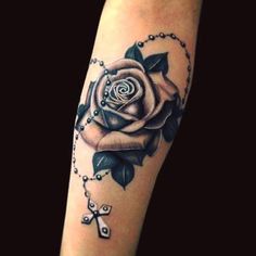 a black and white rose tattoo on the left arm, with rosarys around it