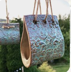 two metal purses hanging from strings in front of some bushes and trees with grass