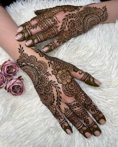 two hands with henna tattoos on them sitting on a white rug next to flowers