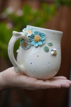 a hand holding a white vase with blue flowers on it