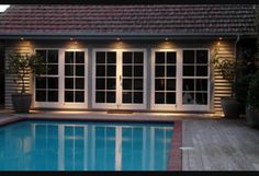 an empty swimming pool in front of a house with large sliding glass doors and windows