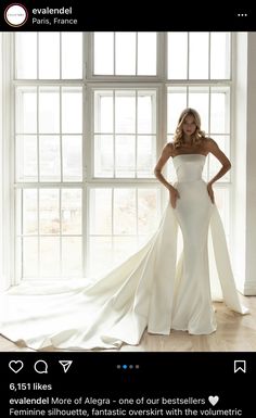 a woman in a white wedding dress standing next to a window with her hands on her hips