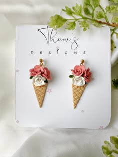 two ice cream cones decorated with flowers on top of a white card next to green leaves