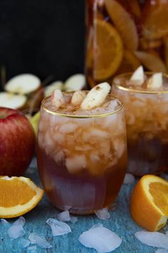 two glasses filled with ice and orange slices next to an apple, another glass full of iced tea