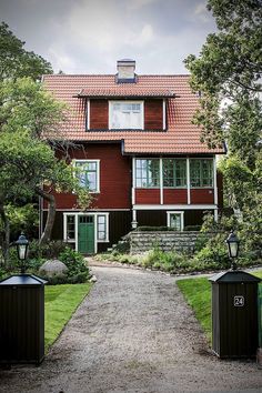 a red house with two black trash cans in the front yard and trees around it