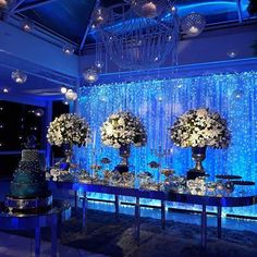 a table topped with lots of white flowers and vases next to a wall covered in blue lights