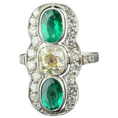 Circa 1910 Vintage Emerald and diamond ring set in Platinum. Ring features two oval shaped Emeralds with a carat weight of approximately 1 carat each, for a total of 2 carats. The Center Old Mine Cut Diamond has a weight of 1.40 carats, K-L color, SI Clarity. Surrounding the three center stones are 14 single cut diamonds with a weight of 0.60 carats. 2.00 carats total diamond weight. Ring size is 6. Emerald And Diamond Ring, Nouveau Jewelry, Diamond Ring Set, Art Nouveau Jewelry, Diamond Ring Settings, Platinum Ring, Vintage Ring, 2 Carat, Emerald Ring