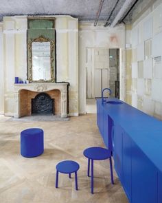 an empty room with blue tables and stools in front of a fire place on the wall