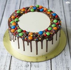 a white cake with chocolate and candy toppings on the top is sitting on a gold plate