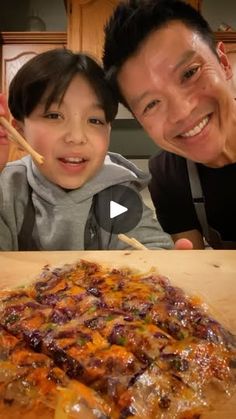 a man and child are smiling at the camera while they eat pizza with chopsticks in front of them