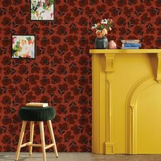 a yellow cabinet and stool in front of a red wallpapered room with pictures on the wall