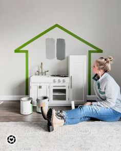 a woman sitting on the floor in front of a house painted with green and white paint