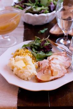 a white plate topped with meat and veggies next to two glasses of wine