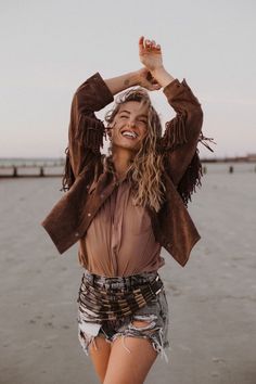 a woman standing on the beach with her arms in the air and smiling at the camera