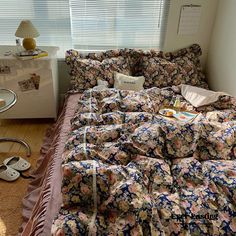 an unmade bed with floral sheets and pillows on the floor in front of a window