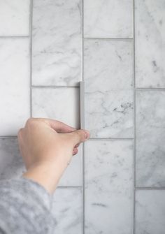 a person's hand is pointing at a white marble tile pattern on the wall