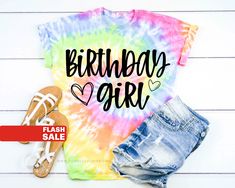 a tie dye birthday girl shirt with shorts and sandals on the floor next to it