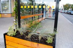 a wooden planter filled with plants sitting on top of a sidewalk next to a building