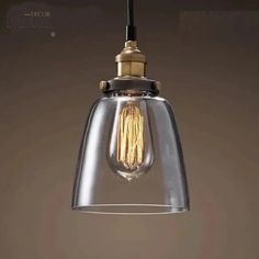 a clear glass light fixture hanging from a black wire with a gold colored bulb on it