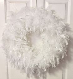 a white wreath hanging on the front door with feathers all over it's frame