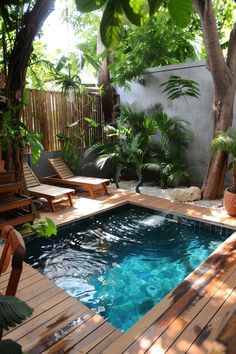 a small pool surrounded by wooden decking and tropical trees in the back yard area