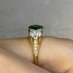 This three-stone ring features a 1.65 carat natural emerald, round cut and set in prongs. On either side of the center stone are old European cut diamonds with a combined weight of 1.08 carats, K-L color and VS1 clarity. Smaller old European cut diamonds are set on the prongs on either side of the emerald and along the shoulders. The under-gallery is decorated with an openwork design. This ring is handcrafted in platinum on 18k yellow gold.
The approximate measurements of the emerald are 7.50mm Heirloom Green Emerald Ring With Three Stones, Heirloom Style Three Stone Green Emerald Ring, Elegant Green Three-stone Emerald Ring, Green Three-stone Emerald-cut Emerald Ring, Luxury Heirloom Three-stone Emerald Ring, Estate Diamond Jewelry, Zambian Emerald, Baguette Cut Diamond, European Cut Diamonds