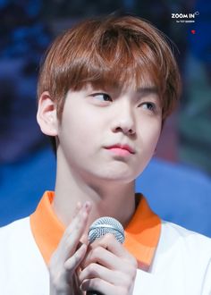 the young man is holding a microphone in his hand and wearing an orange collared shirt