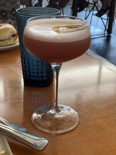 a drink sitting on top of a wooden table next to a plate of food and utensils