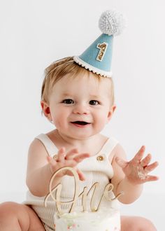 a baby sitting in front of a cake wearing a birthday hat