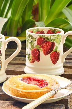 two mugs with strawberries on them are next to a plate with a pie