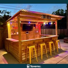 an outdoor bar with stools next to it and lights on the outside wall behind it