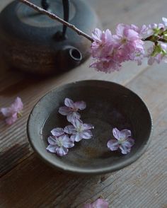 small pink flowers in a gray bowl next to a teapot on a wooden table