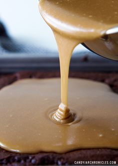 caramel sauce being poured on top of a chocolate cake with a cookie crust in the background