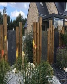 a wooden fence in front of a house with lots of plants and flowers around it