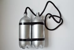 two stainless steel water bottles tied to a black cord on a white wall, with one empty bottle in the foreground