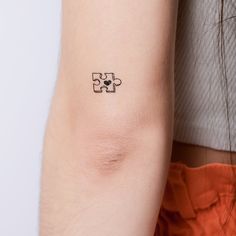 a woman's arm with a small piece of puzzle tattoo on her left arm