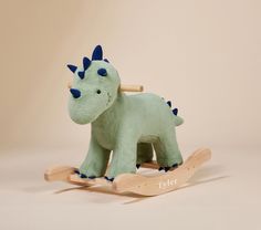 a green toy dinosaur sitting on top of a wooden rocking horse with blue horns and spikes