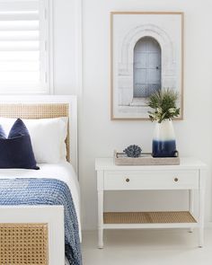 a bedroom with white walls and wicker bedspread on the bed side table