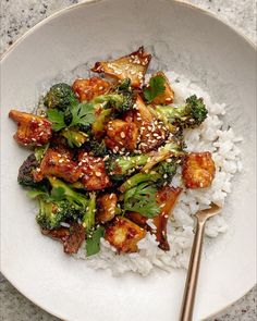 a white plate topped with chicken and broccoli covered in sesame seeds next to rice